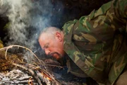 USA, Washington, Olympic National Forest,  Dave Canterbury blows on campfire while camping in Pacific Northwest rainforest during Dual Survivor filming