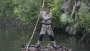 Bear Grylls stands on raft navigating down river using long stick.