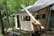 Dixie looks at the camera holding a two by four as he walks past the new addition of the cabin, for the Hiltz cabin, in Kimble Pond, Maine.