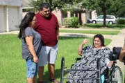 Olivia sitting in her wheelchair taking a break with her brother and sister in law by her side.
