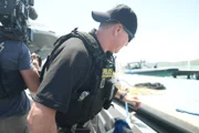 CBP AMO Agent Hud schaut über die Bordwand eines Bootes, während ein Kameramann hinter ihm in Fajardo, P.R. filmt (Lucky 8 TV/Paul Taggart)