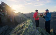 Das einheimische Paar Elisabeth und Fritz Winter aus Westendorf spielen ihre Hörner auf dem Gipfel des Kröndlhorns, während die Sonne an einem wunderschönen Herbstabend untergeht.