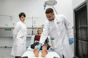 ARD IN ALLER FREUNDSCHAFT - DIE JUNGEN ÄRZTE, neue Vorabend-Weekly mit 42, Folgen 15 "Auf Herz und Nieren", am Donnerstag (21.05.15) um 18.50 Uhr im Ersten. Nach ihrem Autounfall wird Katja Witte (Caroline Scholze, M.) von Dr. Moreau (Mike Adler, r.) und Dr. Koshka  (Katharina Nesytowa, l.) untersucht und über ihre Verletzungen aufgeklärt.