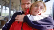 Jörg (R. Viktor Minich) hält mit einer Hand seine Geisel Karin Thaler (Roswitha Meyer) auf seinem Schoss fest und lenkt mit der anderen Hand den Fluchtbus...