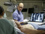 Nachdem auf ihn geschossen wurde, kämpft Gibbs (Mark Harmon, liegend) an Bord eines Krankenschiffes der Navy um sein Leben. Der eigenwillige, aber sehr talentierte Arzt Dr. Cyril Taft (Jon Cryer, stehend) gibt alles, um ihn zu retten ...