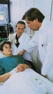 Dr. Roehrs (Siemen Rühaak) und Dr. Stefan Frank (Sigmar Solbach, r.) behandeln Daniel Schillers (Christian Polito) angebliche Sturzverletzung ...