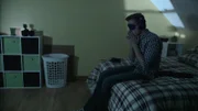 Ein Mann mit einer Augenmaske und Kopfhörern sitzt verängstigt auf dem Bett