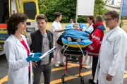 Nach einem Großunfall empfangen Prof. Patzelt (Marijam Agischewa, l.) und Elias (Stefan Ruppe, r.) den Patienten Michael Büker (Sven Gerhard, M.) in der Notaufnahme. Kris Haas (Jascha Rust, 2.v.l.) aus der Sachsenklinik war zufällig am Unfallort und hat Erste Hilfe geleistet (mit Komparsen).