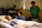 Caro (Annika Schrumpf, l.) liegt auf der Intensivstation. Julia (Barbara Prakopenka, M.)  und Dr. Sandmann (Luca Zamperoni, r.) sind bei ihr.