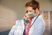 Lisa (Marie Seiser, l.) ist total erschöpft, Dr. von Hatzfeld (Tom Radisch, r.) nimmt sie in den Arm. Sie wurden von einem plötzlichen Ansturm auf die Praxis überrascht. In einem Wettrennen gegen die Zeit versuchen sie hinter die Ursache der mysteriösen Erkrankung zu kommen und die Quarantäne zu beenden.