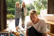 Julian (Ben Münchow, r.) sucht verzweifelt in der Garage nach seinem Stoffelefanten Bobo, während Dagmar (Johanna Gastdorf, l.) und Manju (Alexandra Schalaudek, M.) ihn skeptisch beobachten.