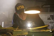 RE-CREATION:  An investigator (played by a background performer) looks closely at pieces from the wreckage on a table in the hanger.   (photo credit:  Cineflix/Ian Watson)