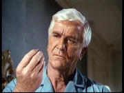 R. R. Benson (Leslie Nielsen) betrachtet die Kugel, an der er hätte sterben können, die aber von seiner Bibel abgefangen wurde.