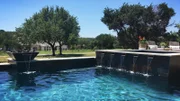 The Pool Kings add scupper water features from the spa and a fire feature/water feature combo pouring water into the pool, creating a calming atmosphere.