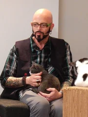 Jackson Galaxy petting a cat in the cafe with staff.