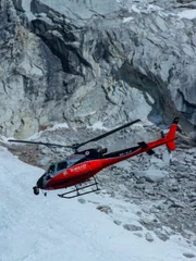 Helicopter flies with snow and rock behind it.