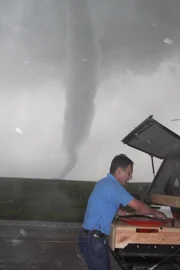 Tim Samaras at vehicle trunk with funnel tornado spinning in background.