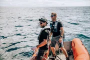 Riley Elliott und Andy Casagrande stehen lächelnd im Rettungsschlauchboot.