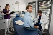 Jasper Beherens (Louis von Klipstein, M.) steht unter Schock. Elias Bähr (Stefan Ruppe, r.) kümmert sich um den jungen Vater, dessen Sohn mit schweren Verbrennungen im künstlichen Koma liegt (mit Komparsin, l.).