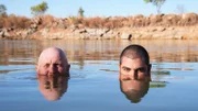 Rod Manning [left] and James "JC" Caruana [right] swimming in a lake with the outback behind them, both looking at the camera, in Western Australia.