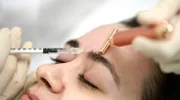 Einer jungen Frau wird von einer Ärztin Botox in die Stirn gespritzt.