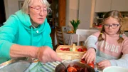 Osterbräuche auf Baltrum: Insulanerin Anneliese Junker zeigt der 11-jährigen Juliane Wagner aus Australien wie sie in ihrer Kindheit die Ostereier mit gekochten Zwiebelschalen gefärbt haben.