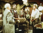 Der Präsident der Eisenbahngesellschaft, Mr. Hollingsworth (Stephen Elliott, l.), bittet Almanzo Wilder (Dean Butler, r.) und Mr. Edwards (Victor French, 2.v.l.) um ihre Mitarbeit bei seinem Projekt.