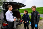 Wolfgang Habedank (Holger Stockhaus, l.) nach der erschütternden Entdeckung des Toten im Wasser. Die Polizisten Süher Özlügül (Sophie Dal, M.) und Henk Cassens (Maxim Mehmet, r.) machen sich Sorgen.