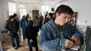 Erik Binz (Tim Oliver Schultz) schreibt in einen Notizblock (Rest: Komparsen).