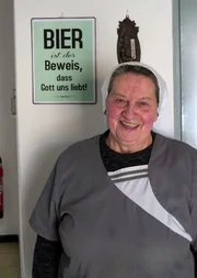 Nonne Doris Engelhard (69) vor Schild mit der Aufschrift "Bier ist der Beweis, dass Gott uns liebt!".