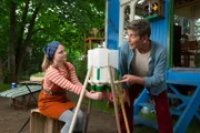 Wer sich vollständig selbst versorgen und einen Kaffee mit Kuhmilch trinken will, der muss melken können. Fritz (Guido Hammesfahr, rechts) zeigt Charlie (Géraldine Raths, links), wie das geht.