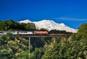 Zug fährt über das Viadukt neben einem schneebedecktem Berg