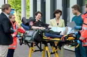 Der Musiker Sebastian Sander (Johannes Franke, M.) hat eine tiefe Schnittwunde am Unterschenkel und wird von Karin Patzelt (Marijam Agischewa, 3.v.r.), persönlich in die Notaufnahme eingeliefert. Marc Lindner (Christian Beermann, l. mit Komparsin) und Mikko Rantala (Luan Gummich, 2.v.r. mit Komparsin, r.) bekommen eine kurze Zusammenfassung über den Zustand des Patienten.