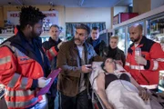 Bei dem Überfall auf Demir Kaplans (Neil Malik Abdullah, 3.v.l.) Laden wurde dessen Tochter Paula (Hannah Bortz) angeschossen. Während Dr. Schmidt (Joel Williams, l.) den aufgeregten Vater beruhigt, warten Sven Riemers (André Röhner, 2.v.l.), Hans (Bruno F. Apitz, M.) und Franzi (Rhea Harder-Vennewald) darauf, ihn befragen zu können.