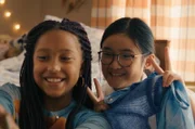 Milli (Marie Ngando, l.) begleitet Châu (Ngoc Nhi Ha Tran, r.) nach der Schule oft mit nach Hause. Dort fühlt sie sich sehr wohl. Milli hat Châu zwei blaue Oberteile geschenkt und macht gleich ein Fotos mit ihrer Sofortbildkamera.