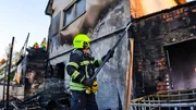 Ein Feuerwehrmann reißt eine Dachrinne an einem ausgebrannten Haus ab
