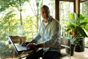 Billy Murdoch (Vincent Regan) sitting at table on laptop.