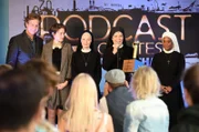 Schwester Agnes (Emanuela von Frankenberg, 3.v.l.), Schwester Hanna (Janina Hartwig, 2.v.r.) und Schwester Lela (Denise M'Baye, r.) bekommen für ihren Klosterpodcast den ersten Preis verliehen. Salm (Thomas Heinze, l.) und Emma Graf (Thekla Hartmann, 2.v.l.) freuen sich mit den Nonnen.