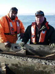 L-R: Juan Ibarra und Freddy Dodge tragen Schwimmwesten, während sie auf einem Boot stehen.