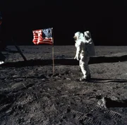Astronaut Buzz Aldrin bei seinen ersten Schritten auf dem Mond. Neben ihm eine animierte USA Flagge.