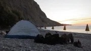 Eine Person ruht sich am Strand neben einem Zelt aus