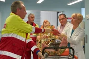 Willy Kröger (Siemen Rühaak, liegend) wird vom Rettungsdienst (li, Komparsen) erneut in die Sachsenklinik eingeliefert. Dr. Kathrin Globisch (Andrea Kathrin Loewig, re.) und Hans-Peter Brenner (Michael Trischan, 2.v.re.) hatten ihn am Vortag mit einer leichten Prellung entlassen. Nun ist er ohnmächtig in seiner Wohnung gefunden worden.