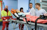 Dr. Kai Hoffmann (Julian Weigend, 2.v.re.) nimmt von der Notärztin (Sarah Arntz, mi.) die kleine Laura Schütz (Lale Andrä, liegend) entgegen. Als Pfleger Kris Haas (Jascha Rust, re.) dazukommt, erkennt er Laura als eine ehemalige Patientin von Dr. Brentano. li.: Komparse