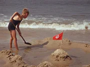 Junge baut Sandburg mit Hakenkreuz-Fähnchen am Strand.