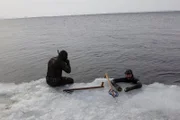 Eric sitting on the ice. Rene Potvin inside the water. Their spears near them on the ice.
