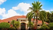 New luxury home with palm trees, flowers, green lawn and lush tropical foliage.