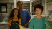 Geschockt starren Hanna (Sannrae Rehnström) und Nina Berger (Denise M’Baye) mit Piet (Noël Lusander) durch die eingeworfene Praxisscheibe.