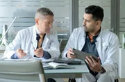 Dr. Ilay Demir (Tan Caglar, re.) hat einen Patienten mit einem Prostatakarzinom und erlaubt sich einen kleinen Scherz mit seinem hochgeschätzten Kollegen Dr. Kaminski (Udo Schenk, li.).