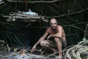 Ed Stafford tending to his campfire while crouching under his shelter in Guatemala.