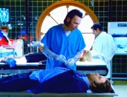 Levine (Ron Silver, liegend), der für tot gehalten wird, versucht mit dem Pathologen Nigel (Steve Valentine) zu kommunizieren, um ihn von der drohenden Obduktion abzuhalten.